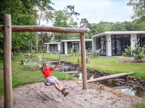 Mädchen schaukelt auf Spielplatz mit modernen Ferienhäusern im Recreatiepark Beekbergen, Gelderland, Niederlande.