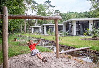Meisje op schommel naast moderne vakantiehuisjes in Recreatiepark Beekbergen, omgeven door groen in Gelderland.