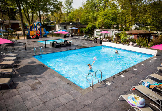 Buitenzwembad en speeltuin in Recreatiepark Beekbergen, vakantiepark in Gelderland, Nederland, zonnig vakantiesfeertje.