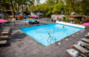 Piscina all’aperto e area giochi al Recreatiepark Beekbergen, villaggio vacanze in Gelderland, Paesi Bassi, giornata soleggiata.