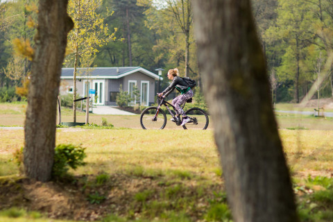Femme à vélo devant un chalet au Recreatiepark Beekbergen, parc de vacances de Gelderland, aux Pays-Bas.