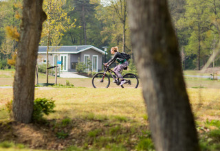 Donna su bicicletta al Recreatiepark Beekbergen, parco vacanze verde a Gelderland, Paesi Bassi, primavera.