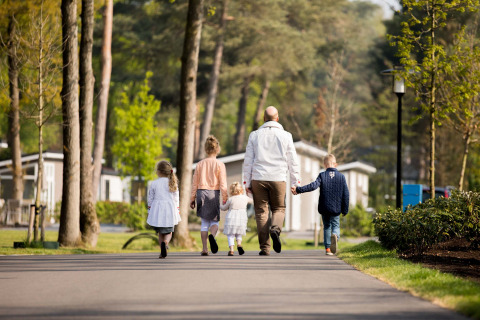 Una familia pasea por el parque vacacional Recreatiepark Beekbergen en Gelderland, Países Bajos, rodeada de árboles.