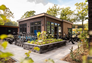 Fietsen en scooters geparkeerd bij een modern gebouw op Recreatiepark Beekbergen, in Gelderland, Nederland.