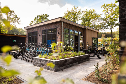 Bicicletas y scooters junto a un edificio moderno en Recreatiepark Beekbergen, parque vacacional en Gelderland, Países Bajos.