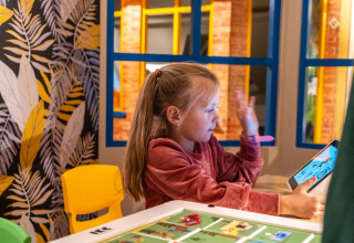 En pige leger med en tablet i et farverigt legerum på Resort Veluwe, en feriepark i Gelderland, Holland.