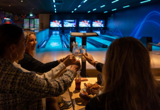 Des amis trinquent avec des boissons et des snacks dans une salle de bowling au Resort Veluwe, Gelderland, Pays-Bas.