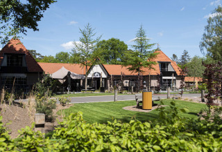 Zicht op Resort Veluwe vakantiedomein in Gelderland, Nederland, met grasveld en roodgedekte gebouwen.