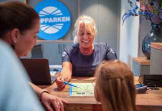 Réceptionniste aidant des clients avec une carte au comptoir du Resort Veluwe, parc de vacances à Gelderland, Pays-Bas.