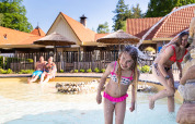 Børn leger i børnepoolen med vandsprøjt på Resort Veluwe feriepark i Gelderland, Holland om sommeren.