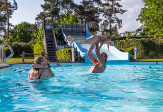 Family playing and enjoying a sunny day at the pool with slide in Resort Veluwe, Gelderland, Netherlands.