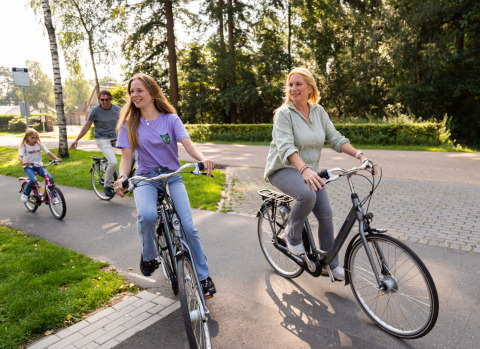 Una familia feliz pasea en bicicleta en Resort Veluwe, un parque vacacional en Gelderland, Países Bajos, rodeados de naturaleza.