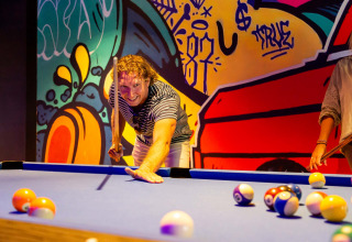 Man speelt biljart in een kleurrijke kamer met graffitiwand bij Resort Veluwe vakantiepark, Gelderland, Nederland.