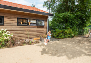 Niño juega en una tirolina en Resort Veluwe, parque vacacional en Gelderland, Países Bajos, junto a edificio y árboles.