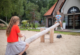 Zwei Kinder spielen auf einer Wippe im Sandkasten vor einem Haus im Resort Veluwe in Gelderland.