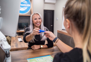 Twee vrouwen geven een sleutel door aan de balie van Bospark Ede, vakantiedomein in Gelderland, Nederland.