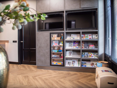 Zona de descanso moderna en Bospark Ede con televisores, revistas, periódicos y juguetes para niños.