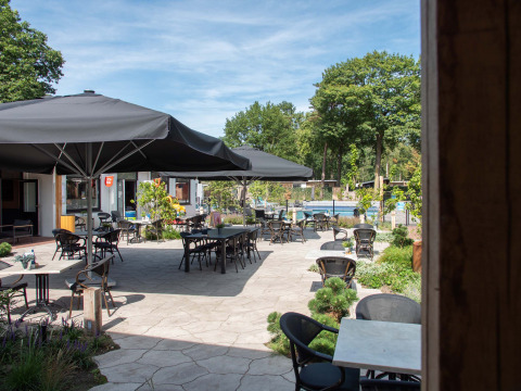 Terraza exterior con mesas, sillas y grandes sombrillas en Bospark Ede, parque vacacional en Gelderland, Países Bajos.