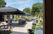 Udendørs terrasse med borde, stole og store parasoller på Bospark Ede, feriepark i Gelderland, Holland.