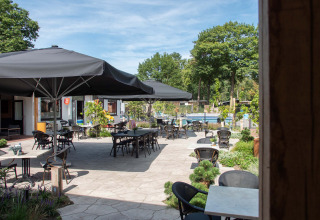 Terraza exterior con mesas, sillas y grandes sombrillas en Bospark Ede, parque vacacional en Gelderland, Países Bajos.
