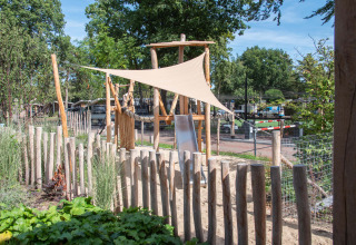 Spielplatz mit Holzumzäunung, Sand und Sonnensegel im Bospark Ede, Ferienpark in Gelderland, Niederlande.