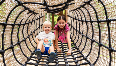 Twee kinderen spelen in een klimtunnel van touw bij Bospark Ede, een vakantiepark in Gelderland, Nederland.