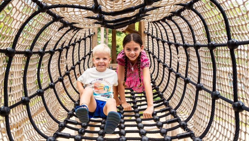 Twee kinderen spelen in een touwtunnel bij Bospark Ede, een vakantiepark in Gelderland, Nederland.