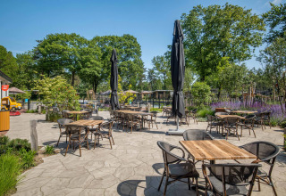 Udendørs caféterrasse med borde, stole og parasoller i Bospark Ede feriepark, Gelderland, Holland.