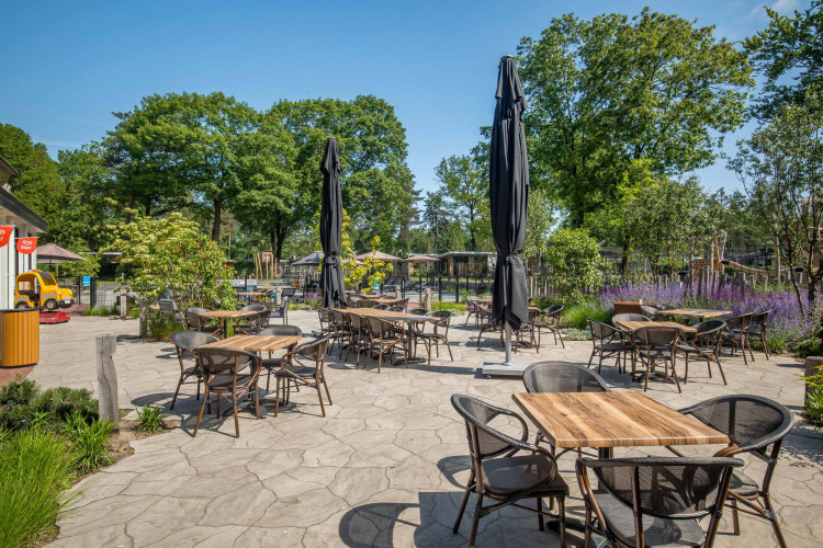 Terraza exterior de cafetería con mesas, sillas y sombrillas en Bospark Ede, un parque vacacional en Gelderland.