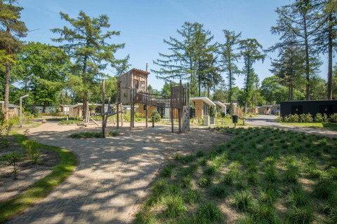 Spielplatz mit Holzhäusern und viel Grün in Bospark Ede, einem Ferienpark in Gelderland, Niederlande.