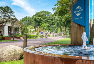 Vakantiepark Bospark Ede in Gelderland, Nederland, met fietsers en een fontein aan het zonnige toegangspad.