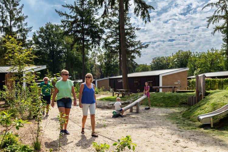 Ferienpark Bospark Ede in Gelderland, Niederlande, mit Erwachsenen beim Spaziergang und spielenden Kindern.