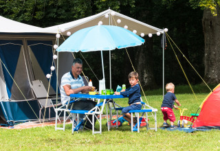 Family enjoys outdoor meal next to tents at Camping La Colline in Belgium Luxembourg, Belgium.