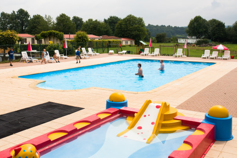 Piscina per bambini con scivolo e lettini al Camping La Colline, parco vacanze nel Lussemburgo belga.
