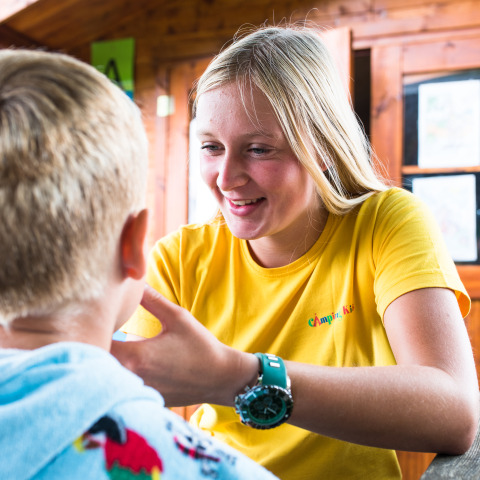 Femme en t-shirt jaune discutant avec un enfant au Camping La Colline, parc de vacances en Belgique Luxembourg.