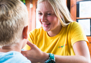 Vrouw in gele T-shirt praat met kind op Camping La Colline, een vakantiepark in Belgisch Luxemburg.