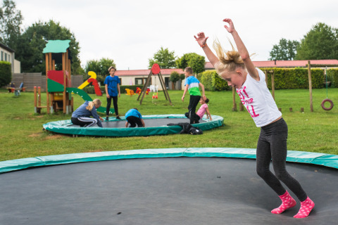 Kinder spielen auf eingelassenen Trampolinen und einem Spielplatz im Camping La Colline, Luxemburg, Belgien.