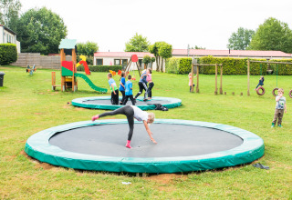 Børn leger på nedgravede trampoliner og legeplads i Camping La Colline, Belgien, omgivet af grønne områder.