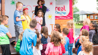 Children enjoy a fun group activity with a costumed adult on stage at Camping La Colline in Belgium.