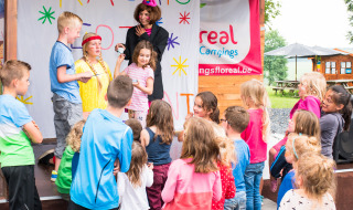 Kinder nehmen an einer fröhlichen Gruppenaktivität mit einem kostümierten Erwachsenen im Camping La Colline teil.