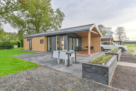 Luxe lodge met sauna bij Drentse Weelde in Nederland, modern buitenterras en een auto geparkeerd naast.