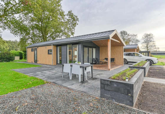 Luxe lodge met sauna bij Drentse Weelde in Nederland, modern buitenterras en een auto geparkeerd naast.
