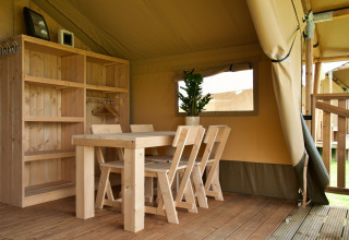 Interno di una tenda safari con mobili e scaffali in legno al Camping La Colline in Belgio, atmosfera accogliente.