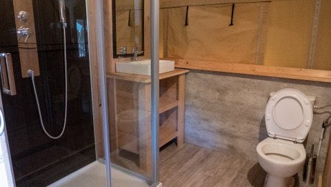 Safari tent bathroom at Camping La Colline in Belgium with shower, sink and toilet visible.