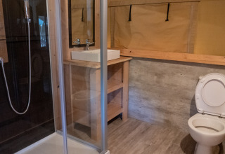 Safari tent bathroom at Camping La Colline in Belgium with shower, sink and toilet visible.