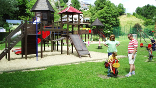 Parque infantil en Camping la Roche en Bélgica, con niños, padres y estructuras de juego de madera.