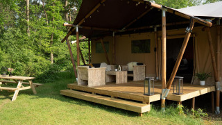 Tienda safari con terraza de madera y zona de estar en Holiday Park Mölke, Países Bajos, rodeada de vegetación.