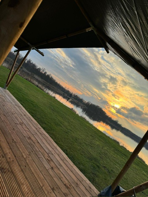 Zicht vanuit een safaritent bij Camping de Kleine Wielen in Nederland, met gras, meer en zonsondergang.