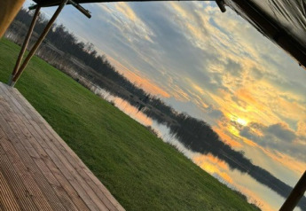 Udsigt fra en safaritelte på Camping de Kleine Wielen i Holland, med sø, græs og solnedgang.