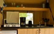 Kitchen area inside a safari tent with stove, fridge, coffee maker, sink, and various utensils.